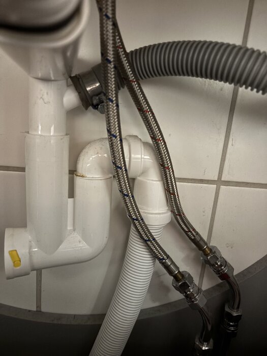 Avlopp och vattenlås under ett handfat i badrummet, med flera rör och slangar anslutna.