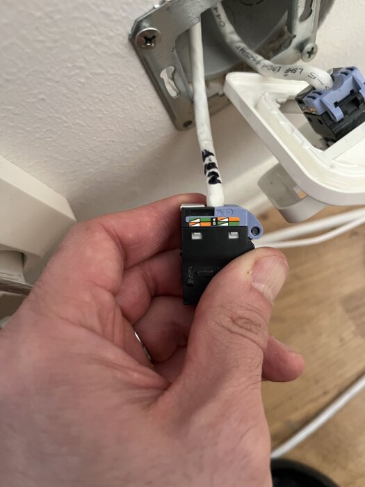 Hand håller en kabeländkoppling med synliga trådar framför ett vägguttag.