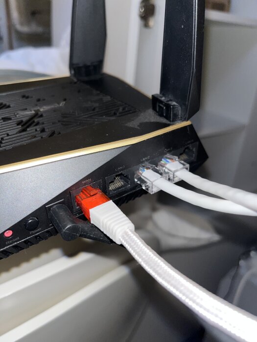 Svart router med antenner och flera nätverkskablar anslutna till LAN- och WAN-portar.