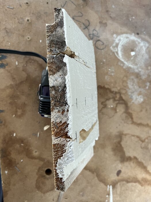 Träbit med sprickor och skador i kanten, liggande på en arbetsbänk med verktyg i bakgrunden.