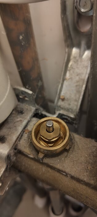 Närbild på en ventil med ett metallstift, del av golvvärmesystem, omgiven av damm. Inlägg handlar om vattenflöde och termostatens funktion.