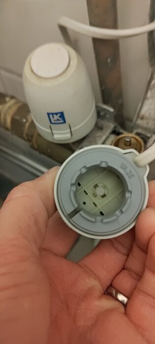 Närbild av en termostatventil från LK med borttagen vit propp, visar stiftet som styr vattenflödet för golvvärme.