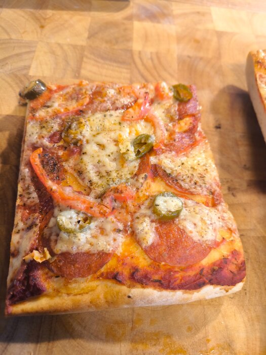 Rektangulär pizza med salami, peperoni, ost, jalapeños och tomatsås på skärbräda.