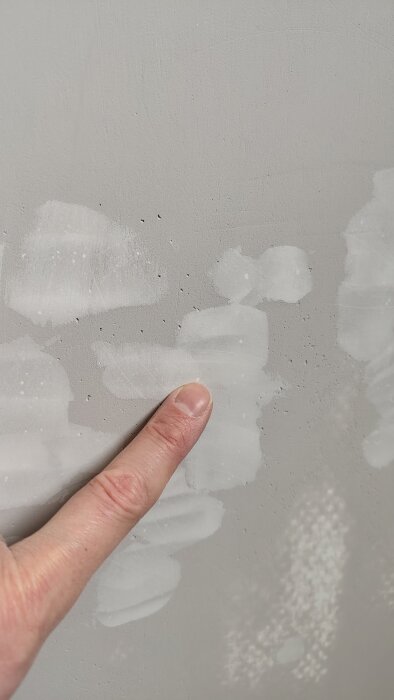 Närbild av en vägg med ojämnheter och små gropar i spacklet. Ett finger pekar för att visa storleken på groparna.
