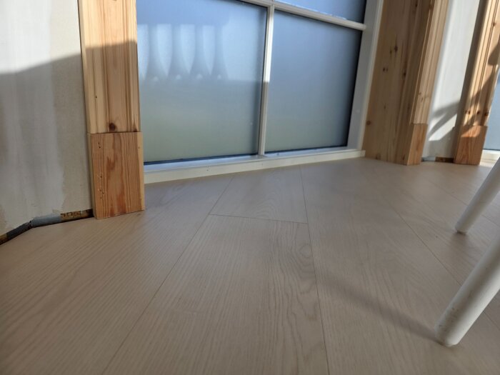 Ljust golv med träpanel och skurklossar vid ett fönster. Lister möter väggen och funderas över renoveringens estetik.