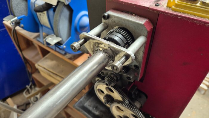 Materialstöd för långa ämnen, monterat på en minisvarv, visar en metallstång fixerad med bultar och kugghjul i bakgrunden.