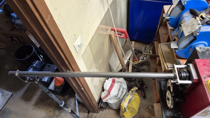 Materialstöd för långa smala ämnen på minisvarv i verkstad, omgiven av verktyg och byggmaterial, som cement och slipmaskin.