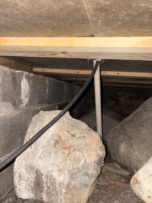 Stenblock och kablar under en byggnad, grunden saknar inspektionslucka. Bild tagen genom grävning under en stuga med mögelluktproblem.