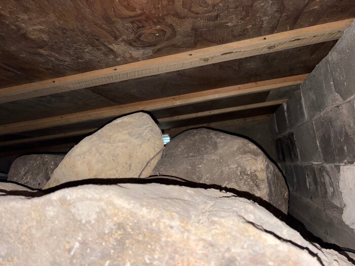 Stora stenblock under en stuga, synliga vid grävning, med en grund bestående av en plywoodbotten och murade väggar.