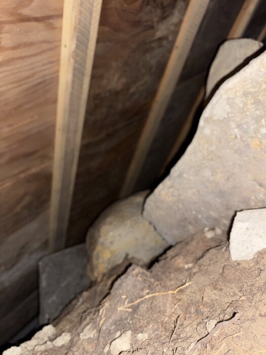 Under stugan syns stora stenblock och träbjälkar i en grund utan inspektionslucka, vilket kan orsaka mögelproblem.