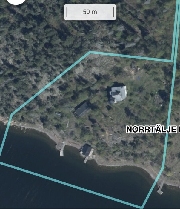 Flygbild över ett skogsområde vid en kustlinje med hus och bryggor, omgiven av markerade gränser.