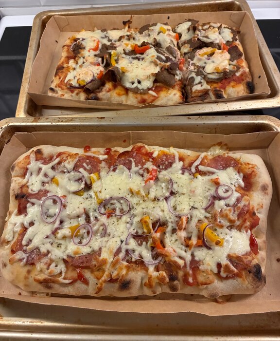 Två pizzor på bakplåtar: övre med kebab och blandad sås, nedre med salami, ost, rödlök och paprikabitar.