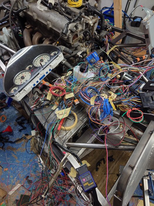 Motordel med omfattande kabeldragning, en OBD-skanner och mätardisplay i ett garage, redo för uppstart efter renovering av tankarmatur.