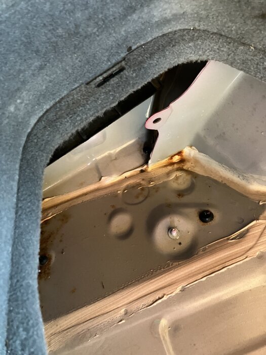 Inre fack i bagageutrymmet på en Prius -07 där vatten har samlats, med synliga rostfläckar och en plastkant.
