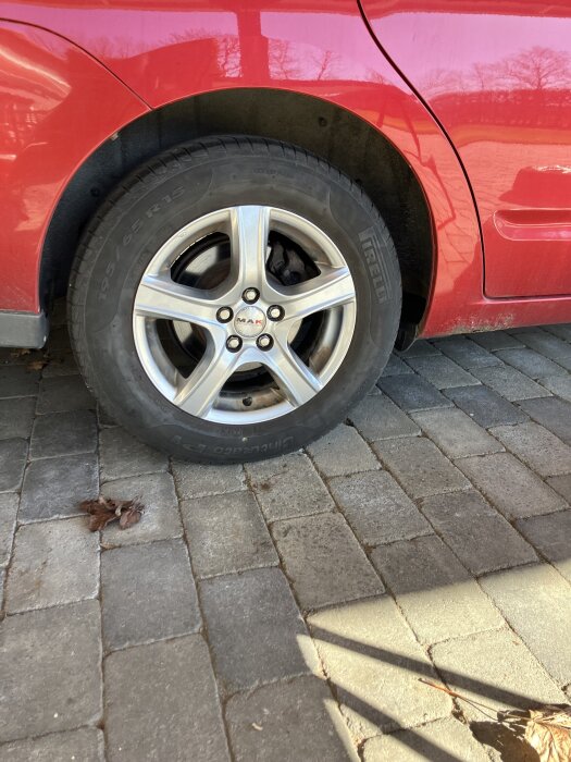 Rött bilhjul med Pirelli-däck och silverfälg, parkerad på stenlagd uppfart.