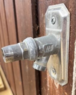 Äldre vattenutkastare monterad på trävägg, söker rörböj för att ändra utgående vattenflödets vinkel.