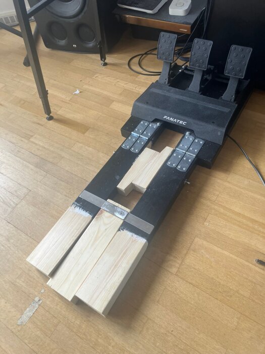 Hemmagjord pedalställning med trä- och metallkonstruktion, designad för stabilitet vid hårda inbromsningar. Syns ihopvikt på golvet.
