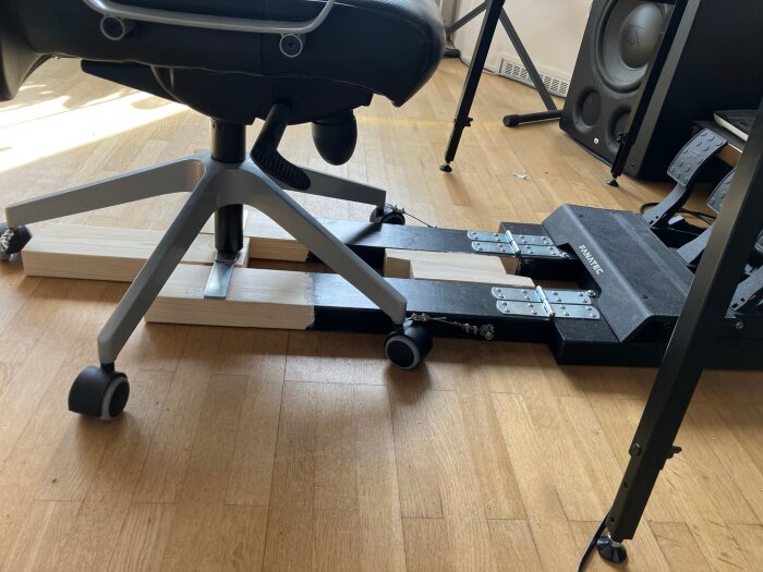 Byggprojekt för att stabilisera stolen vid bromsning, med trä- och metallkonstruktion under stolsbenen på ett trägolv.