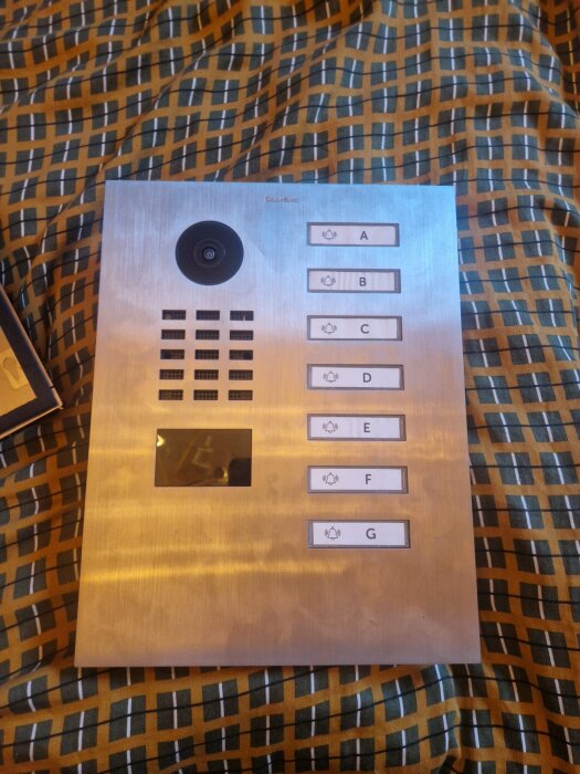 Intercom med sju knappar och kamera placerad på ett mönstrat tyg.