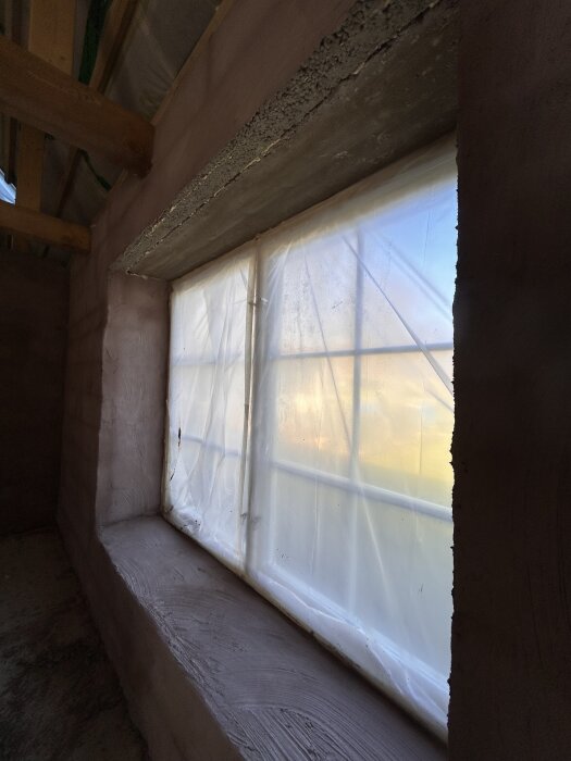 Fönster med plastöverdrag och putsade ytor, inklusive undersida ovanför fönstret, i ett hus som är under renovering.