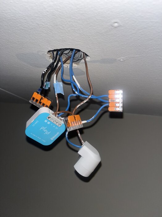 Elektrisk installation med Plejd-enhet och flera kopplingssladdar synliga i taket. Sladdar i olika färger anslutna till en kopplingsdosa.