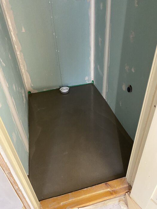 Nylagt golv avspolat betong i ett duschutrymme med vattenlås och gipsskivor på väggarna. Förberedelse för kakling och andra ytskikt.