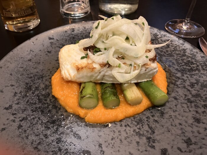 Grillad torskfilé serverad på en bädd av morotspurè med sparris och garnerad med tunt skivad lök.