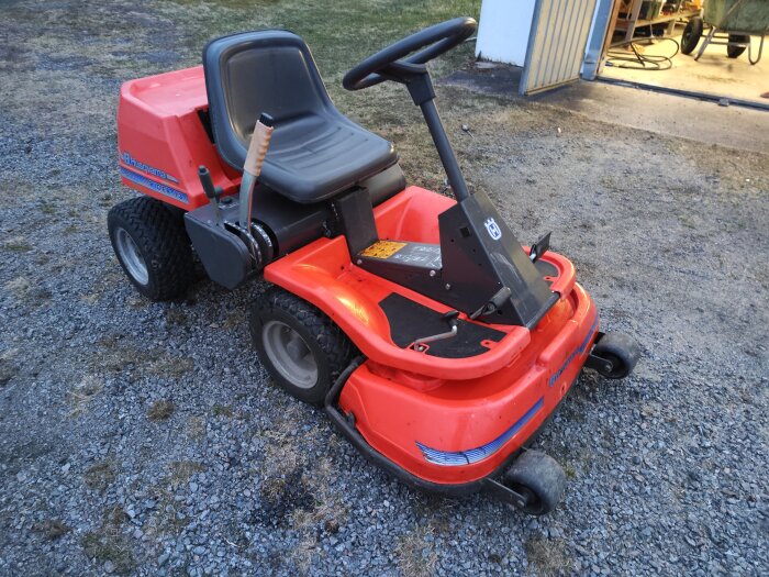 Gräsklippare av märket Husqvarna står på en grusuppfart framför ett öppet garage.