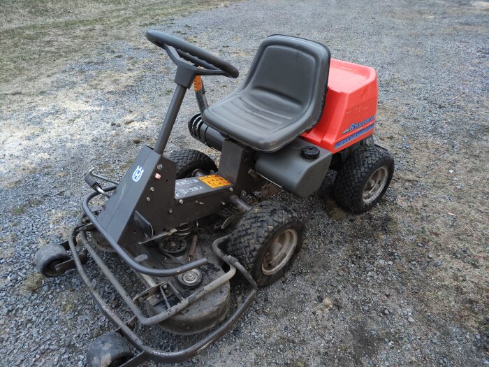 En röd och svart Husqvarna åkgräsklippare som står på en grusplan.