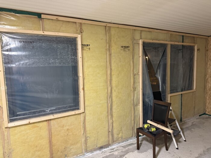 OSB-skivor och plastfolie på vägg för golvventilation, träramar runt fönster, verktyg på stol.