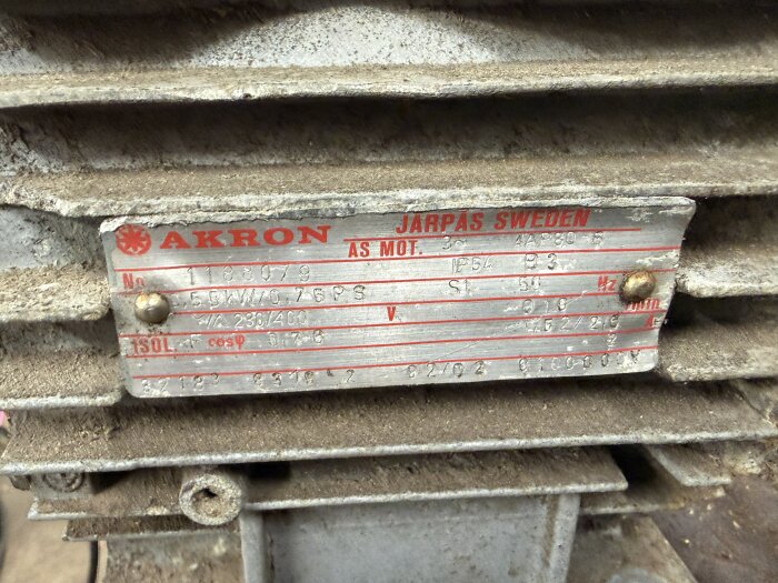 Dammig namnskylt på en motor med texten "AKRON JÄRPÅS SWEDEN", visar teknisk information som modellnummer och elektriska specifikationer.