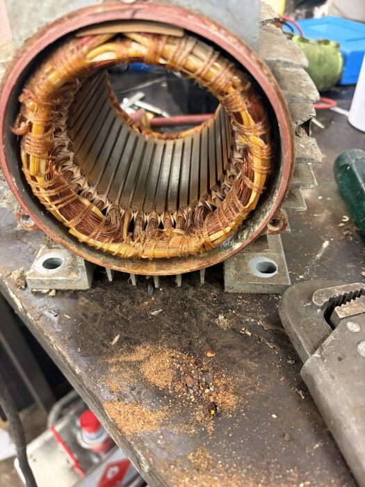 Närbild på insidan av en elektrisk motor med kopparlindningar, placerad på ett arbetsbord med verktyg och metallspån runt omkring.