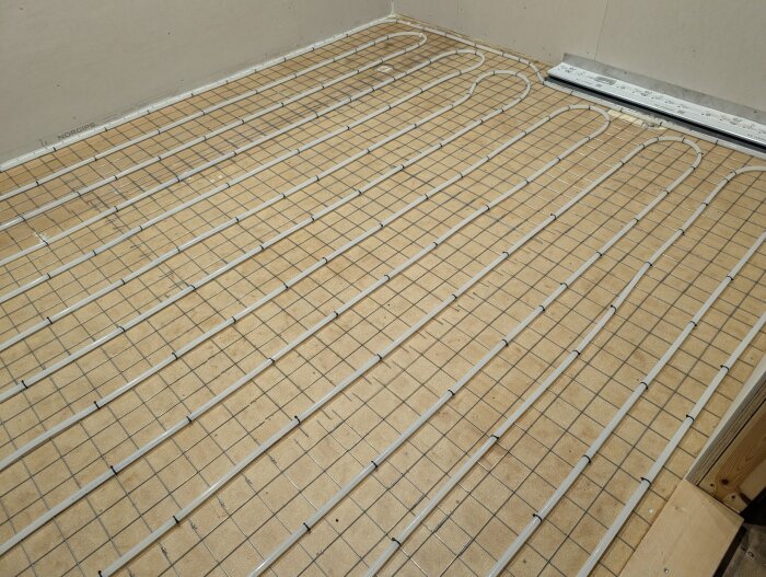 Golvbjälklag med inlagd golvvärmeslang och nät på spånskiva för badrumsrenovering.