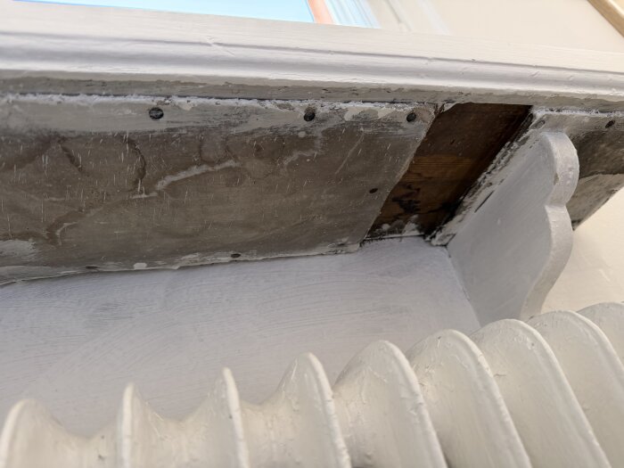 Material under fönsterbräda, misstänkt eternit, i gammalt hus från tidigt 1900-tal. Materialet är fastspikat och visas ovan en vitmålad radiator.