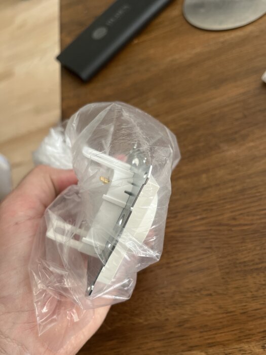 Strömbrytare i plastförpackning hålls i en hand över ett träbord.