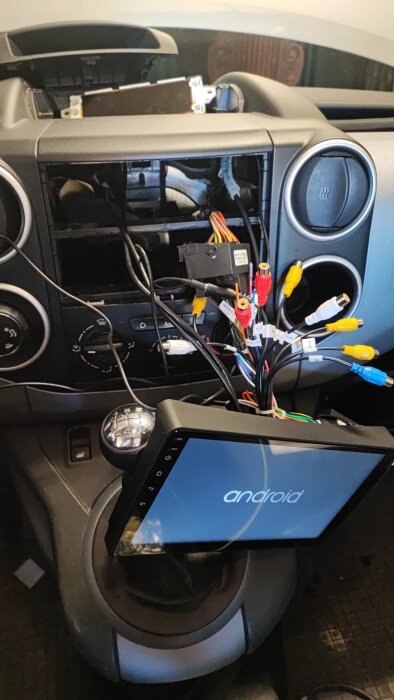 Bild av en bilinteriör med instrumentpanel där en eftermarknads stereo med Android installeras och kablar är anslutna.