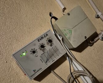 Kontrollpanel med tre rattar och lysdioder, monterad på en vägg bredvid en kopplingsdosa.