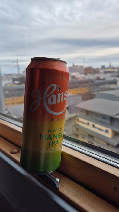 Burk med Hansa Mango IPA på ett fönsterbräde med utsikt över Oslo stad.