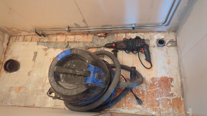 Dammsugare och borrmaskin på ett delvis rivet golv, förberedelser för renovering.