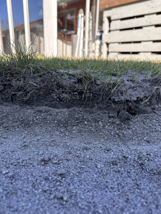 Närbild av jordlager med gräs ovanpå, intill en byggnad. Markarbete förbereds för att lägga matjord och rulla ut gräs.