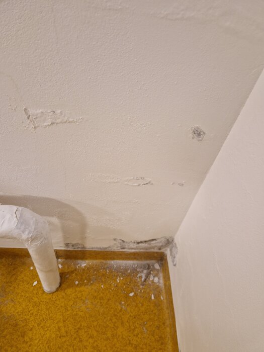 Färgflagor vid källarhörn med rör, tecken på fuktproblem i 70-tals hus.