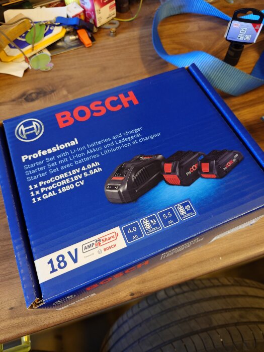 Kartong med Bosch Professional batteri- och laddarset, 18V, på ett bord med verktyg och tillbehör i bakgrunden.