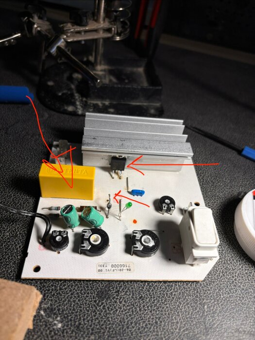 Kretskort med olika elektroniska komponenter, inklusive en kylfläns, triac och droppkondensator. Röda pilar markerar specifika delar.
