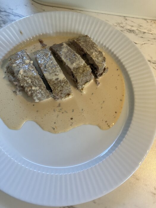 Skivad köttfärslimpa med sås på en vit tallrik.