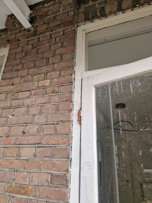 Originaldörr med glasruta från 1925, monterad i tegelvägg, visar slitage på karmen och icke-drevat utrymme mellan karm och vägg.