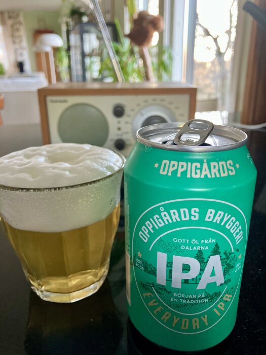 Grön burk med Oppigårds IPA och ett glas öl med skum, i ett kök med radio och växter i bakgrunden.