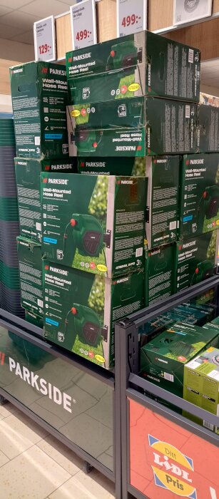 Flera kartonger med Parksides väggmonterade slangvindor staplade på en hylla i en butik. Prisskyltar synliga ovanför.