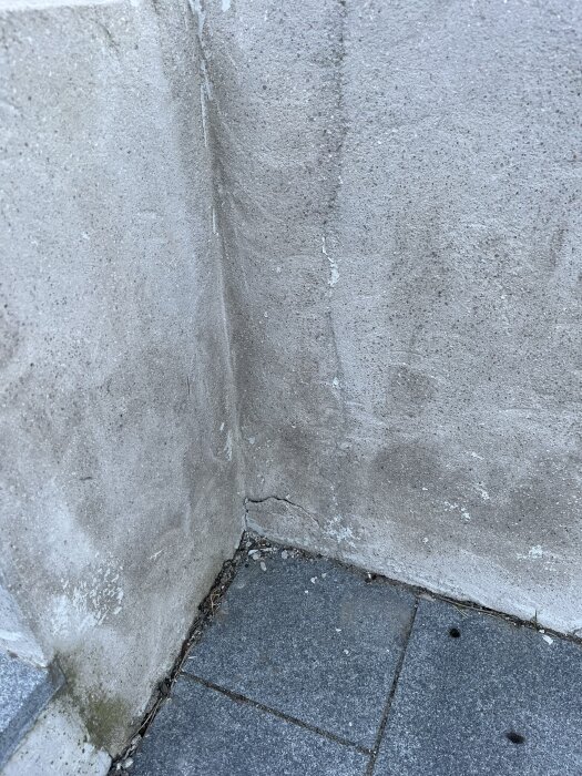 Spricka i murad vägg vid hörn, synlig vid övergången till stenbelagd markyta.