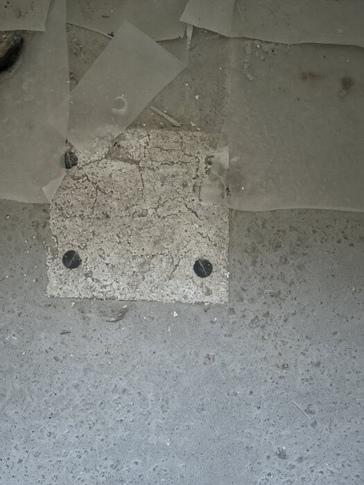 Frigolitkub ingjuten i betongplatta på mark, täckt med plastfolie, med synliga skruvhuvuden; sannolikt plats för golvbrunn.