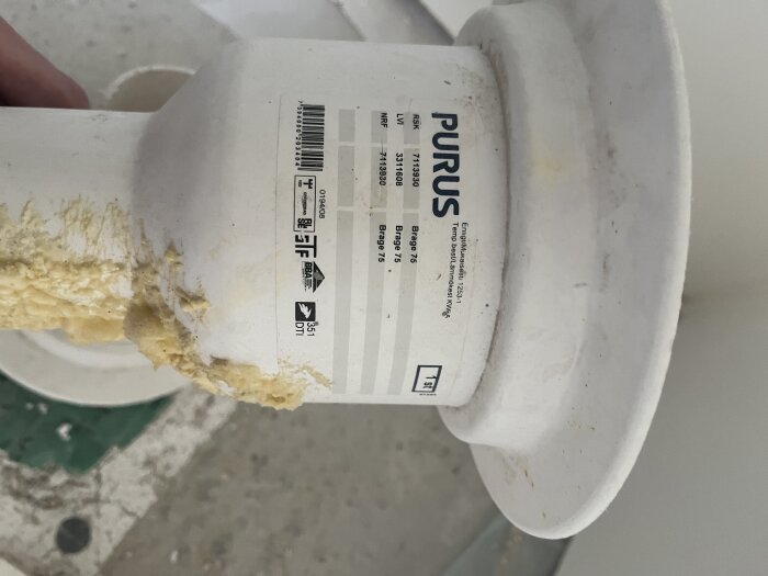Golvbrunn från märket Purus med bottenutlopp ligger på ett underlag. Text och etikett syns tydligt på sidan av brunnen.